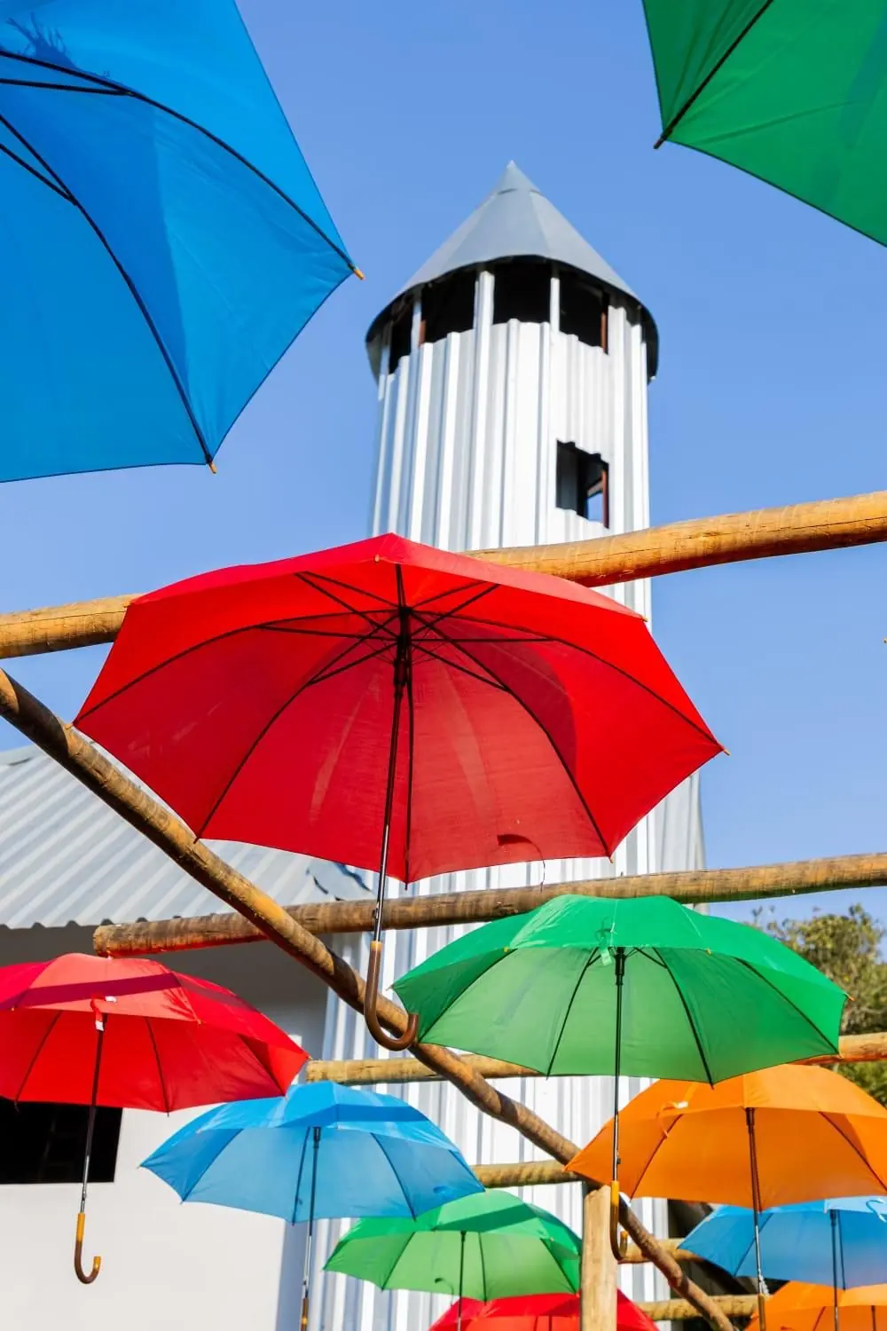 Corredor de guarda-chuvas coloridos suspensos com a torre branca do rancho ao fundo