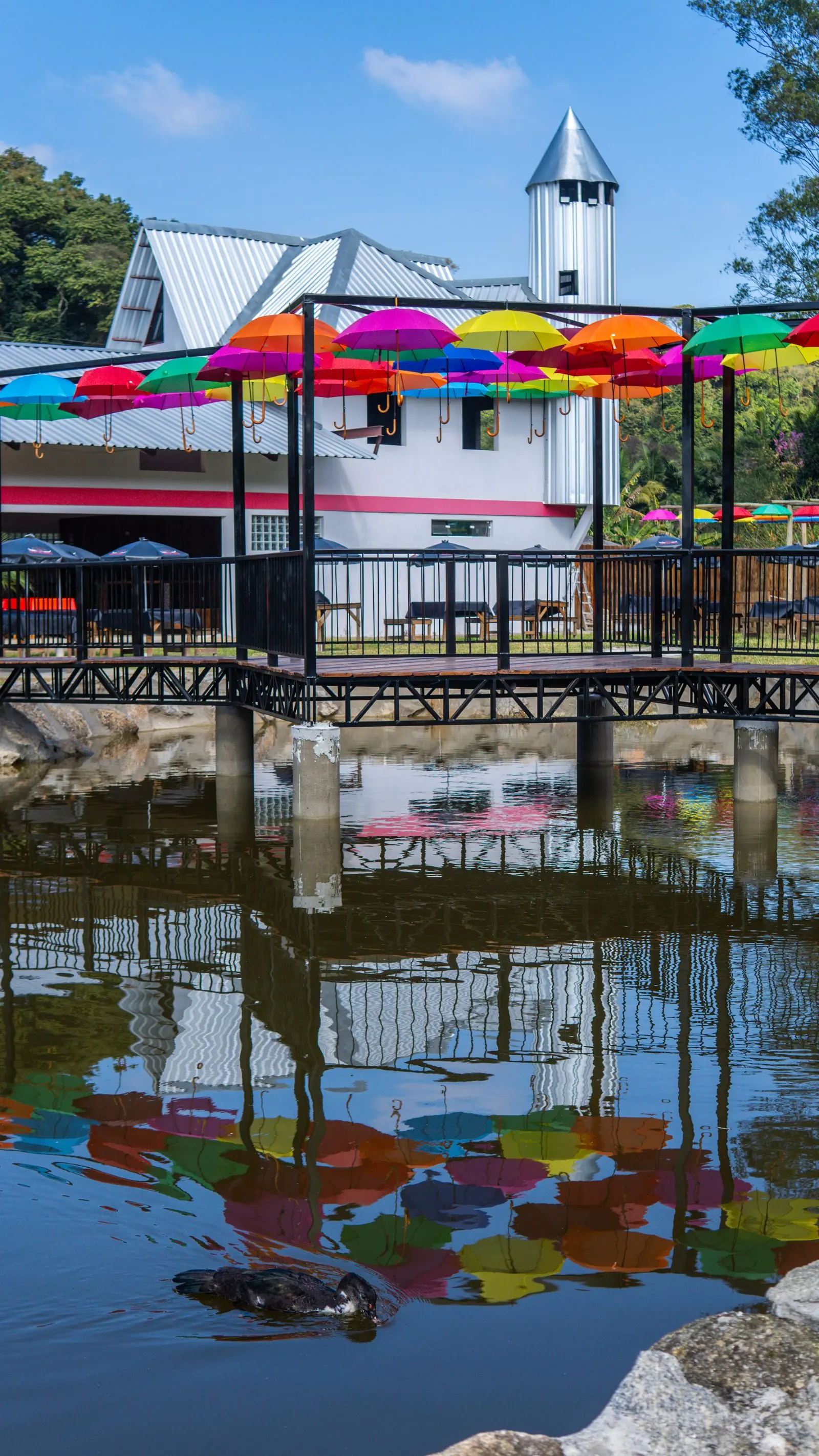 Lago do Rancho Santa Inês com o reflexo dos guarda-chuvas coloridos e do salão branco na água