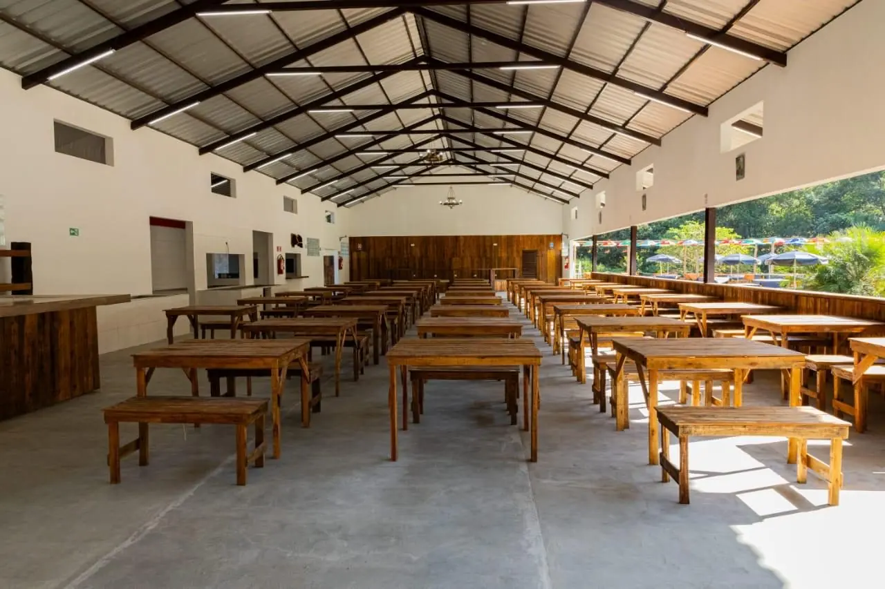 Salão coberto com mesas de madeira preparado para receber eventos